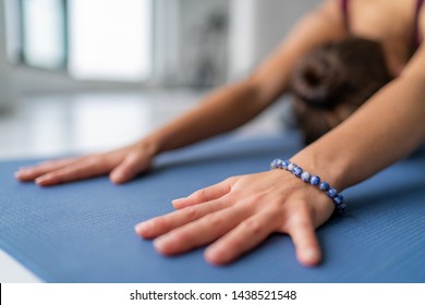 Yoga meditation woman doing childs pose stretching in gym studio or living room home. Closeup of hands touching floor exercise mat and bracelet. Fitness wellness concept.