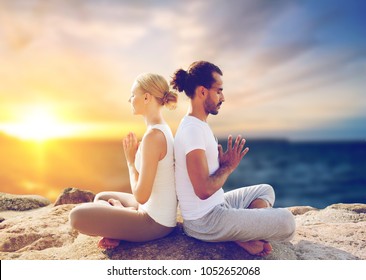 yoga , mindfulness, harmony and people concept - happy couple meditating in lotus pose outdoors over sea background - Powered by Shutterstock