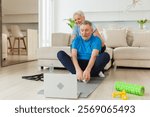 Yoga mindfulness meditation. Senior adult mature couple practicing yoga with online lessons in laptop. Old wife helping teaching husband meditating relaxing. Family doing breathing practice at home