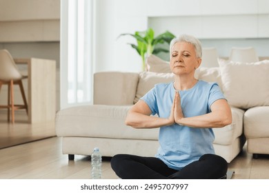 Yoga mindfulness meditation. Senior adult mature woman practicing yoga at home. Mid age old lady sitting in lotus pose on yoga mat meditating relaxing. Older middle aged woman doing breathing practice - Powered by Shutterstock