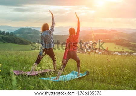 Yoga in nature, fresh air in park. Group of sporty women practicing pose together, stretching health on top of mountain in meadow at sunrise, zen wellness. Teamwork, good mood and healty life.