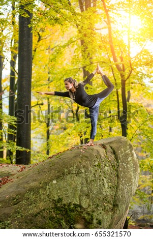 Yoga outdoors - sporty fit woman doing asana Narajasana in autumn park on the big boulder
