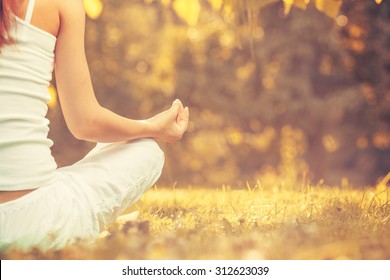 Yoga Outdoors In Warm Autumn Park. Woman Sits In Lotus Position Zen Gesturing. Concept Of Healthy Lifestyle And Relaxation