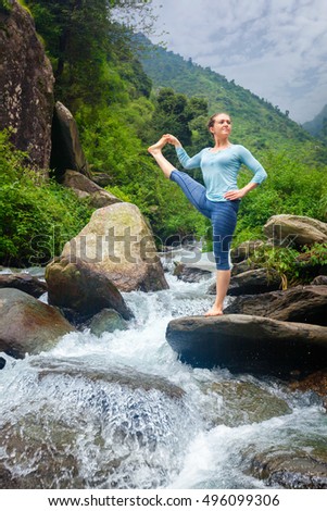 Yoga outdoors - woman doing Ashtanga Vinyasa Yoga balance asana Utthita Hasta Padangushthasana - Extended Hand-To-Big-Toe Pose position posture outdoors at waterfall