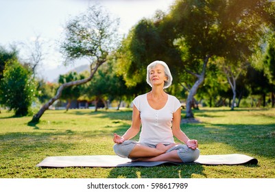 Yoga at park. Middle age woman in lotus pose sitting on green grass. Concept of calm and meditation.