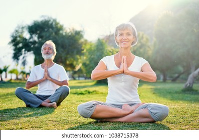 Yoga at park. Middle aged family couple  sitting in lotus pose on green grass. Concept of pray and meditation.