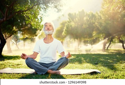 Yoga at park. Senior bearded man in lotus pose sitting on green grass. Concept of calm and meditation. - Powered by Shutterstock