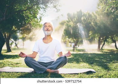 Yoga at park. Senior bearded man in lotus pose sitting on green grass. Concept of calm and meditation.