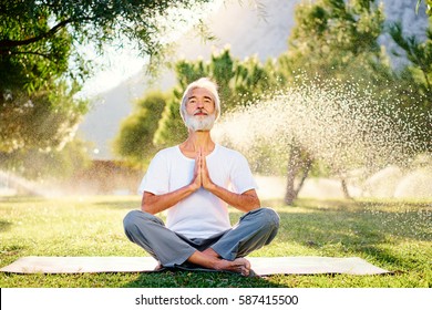 Yoga at park. Senior bearded man in lotus pose sitting on green grass. Concept of pray and meditation.