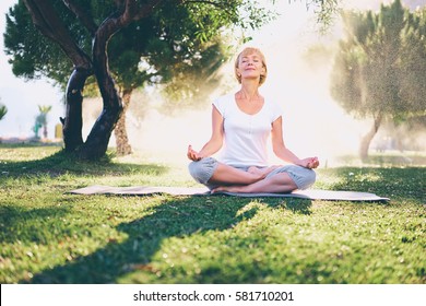 Yoga at park. Senior woman in lotus pose sitting on green grass. Concept of calm and meditation.