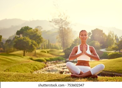 Yoga at park with view of the mountains, with sunlight. Young woman in lotus pose sitting on green grass. Concept of calm and meditation. - Shutterstock ID 753602347