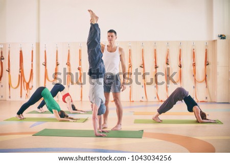 Yoga practice, instructor helping student to do handstand in class, Adho Mukha Vrikshasana, Downward facing Tree Pose, group of people working out in sports club, full length