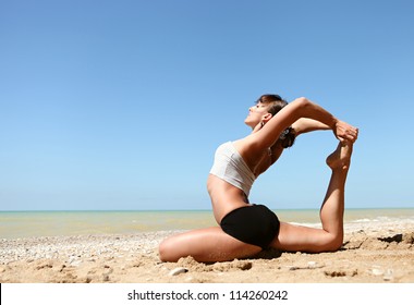 Yoga practice. Young girl doing king pigeon yoga pose on the beach - Powered by Shutterstock