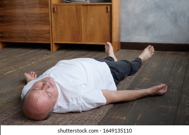 Yoga. Senior man meditating on a wooden floor and lying in Shavasana pose. Attractive yogi working out at home, doing yoga