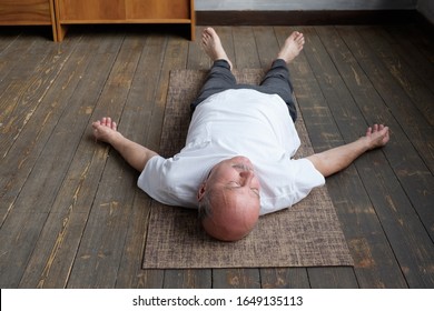 Yoga. Senior man meditating on a wooden floor and lying in Shavasana pose. Attractive yogi working out at home, doing yoga