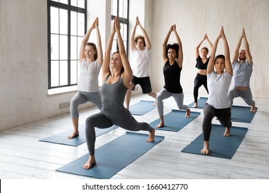 Yoga session led by caucasian woman coach, millennial athletic multiracial group of people practising posture with female instructor, doing Warrior one Virabhadrasana I asana, workout full length view - Powered by Shutterstock