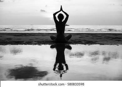 Yoga Silhouette. Woman Doing Meditation Near The Ocean Beach. Black And White Photo.