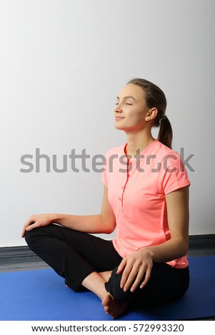 Yoga smiling girl sitting with legs crossed, her hands on feets. Eyes closed
