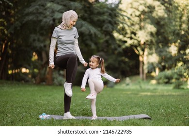 Yoga and stretching exercises of mom with child outdoors. Likable young Muslim mother and her cute daughter, having outdoor workout in the park, standing on yoga mat and doing high stepping exercise - Powered by Shutterstock