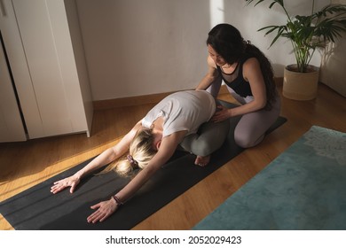 Yoga teacher correcting a woman's back stretching position at home