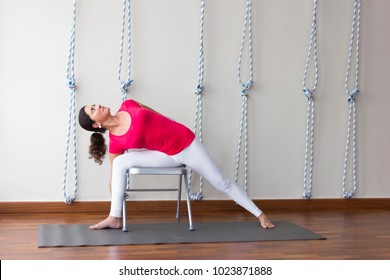 Yoga teacher practicing in studio with chair as prop to help on demanding pose. Yogi class concept, instructor shows variation for flexibility