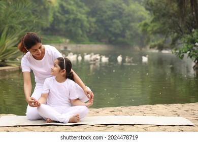 A Yoga Teacher Teaching Yoga Poses To Her Student Beside A Lake In A Park For Good Health In A Serene Atmosphere. 