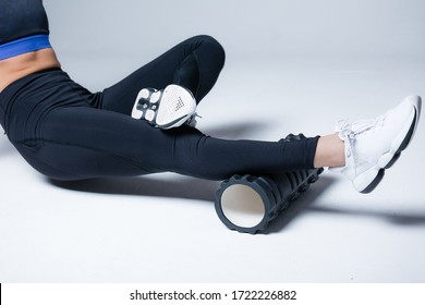 Yoga trainer kneads fascia of the calf muscle with black massage roller, sitting on the floor. Exercising muscles before training