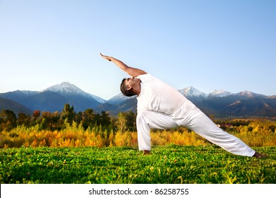 Yoga utthita parsvakonasana triangle pose by happy Indian Man in white cloth in the morning at mountain background