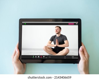 Yoga video class. Online meditation. Virtual training. Woman hands holding tablet with relaxed man in lotus pose on screen isolated on blue.