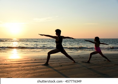 Yoga Virabhadrasana II (Warrior II Pose) By Mom And Daughter In Silhouette With Sunset Sky Background