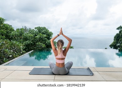 Yoga woman meditating doing praying hands pose at yoga retreat near infinity swimming pool. Summer vacation relaxation. Back view
