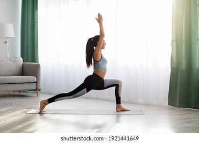Yoga woman in sportswear exercising at home, standing in warrior pose on fitness mat, side view, copy space, full length shot. Healthy, sporty lifestyle, yoga practicing at home during self-isolation - Powered by Shutterstock