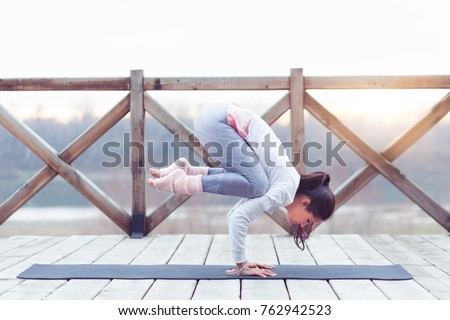 Yoga woman strength training on exercise mat doing yoga poses exercises at nature. Difficult pose, asymmetrical arm balance and hanstanding asana or Angle Pose.