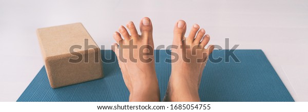 Yoga woman stretching feet spreading her toes doing\
toe stretch on exercise mat of living room floor at home. Foot\
exercises stretches fun.