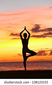 Yoga Woman Training In Sunset In Tree Pose Meditating Outdoors By Beach Ocean Sea. Female Yoga Instructor Working Out Training In Serene Ocean Landscape. Silhouette Of Woman Model Against Sun.