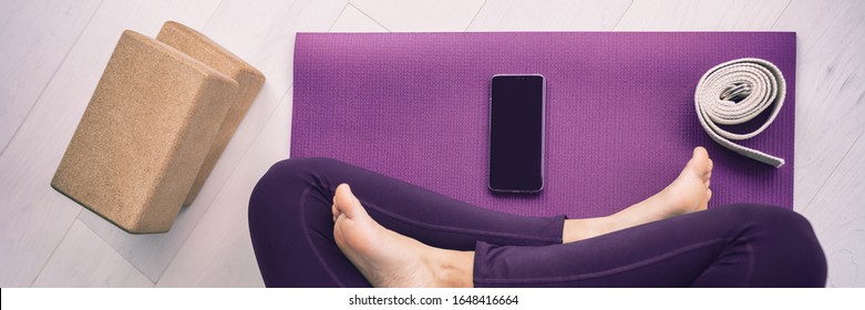 Yoga woman using mobile phone panoramic banner top view of cellphone on exercise mat and blocks, stretching strap. - Powered by Shutterstock