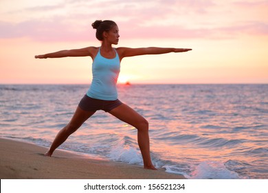 Yoga woman in zen meditating in warrior pose relaxing outside by beach at sunrise or sunset. Female yoga instructor working out training in serene ocean landscape. Big Island, Hawaii, USA.