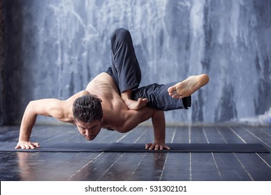  Yoga. Junge Mann, der eine asana ashtavakrasana macht. Hand stehende Pose. Yogi Master Training auf schwarzer Matte im urbanen Studio. Yoga-Indoor in der Nähe eines Fensters, Lifestyle-gesundes Konzept
