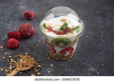
yoghurt with granola and fruit in a plastic glass on a black background. Food delivery. healthy food