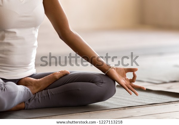 Yogi black woman practicing yoga lesson,\
breathing, meditating, doing Ardha Padmasana exercise, Half Lotus\
pose with mudra gesture, working out, indoor close up. Well being,\
wellness concept