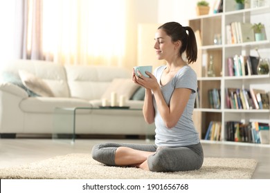 Yogi drinking tea after yoga exercises sitting on the floor at home