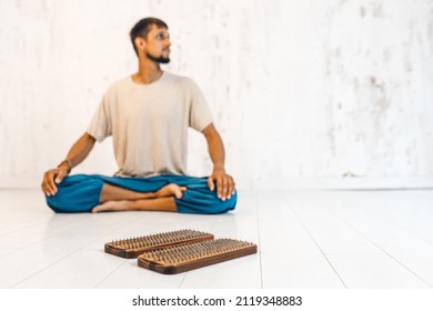 A yogi in the lotus position meditates next to a sadhu board. Board with nails ready for practice of standing on nails on white background