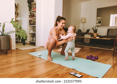 Yogi Mom Lifting Her Baby On An Exercise Mat. Happy Mother Smiling Cheerfully While Working Out With Her Baby At Home. New Mom Bonding With Her Baby During Her Post-natal Fitness Routine.