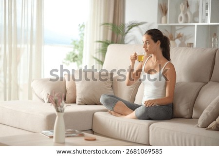 Yogi resting drinking tea after yoga exercises sitting on a couch at home