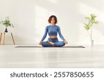 Yogi sporty attractive woman practicing yoga on white floor, doing Ardha Padmasana exercise, meditating calm in Half Lotus pose doing mudra gesture in home sport or modern studio fitness for health