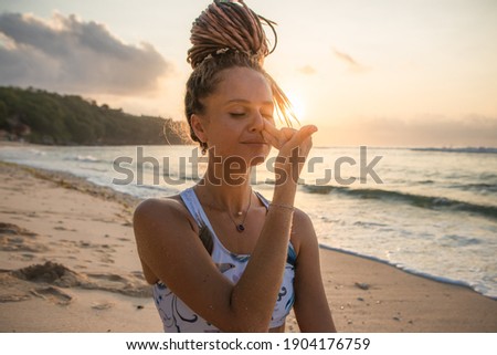 Yogi woman practicing Nadi Shodhana Pranayama, Alternate Nostril Breathing. Control prana, control of breath. Breathing exercise. Self care concept. Sunset time. Yoga retreat. Thomas beach, Bali