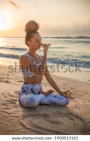 Yogi woman sitting in lotus pose, practicing Anuloma Viloma Pranayama, Alternate Nostril Breathing. Control prana, control of breath. Breathing exercise. Sunset time. Yoga retreat. Thomas beach, Bali