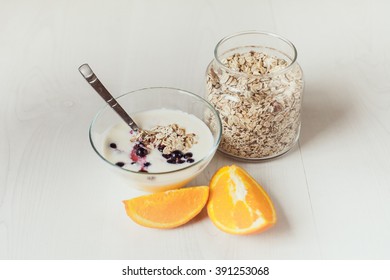 Yogurt with berries currants, a spoon, a jar with oat flakes and orange on a light table.
