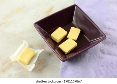 Yogurt Chewy Candy Pieces In Purple Bowl And One In Opened Candy Wrapper With Lavender Napkin