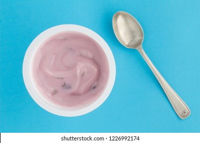 Yogurt cup with strawberry yoghurt in small plastic cup and vintage silver spoon on bright blue background - top view photo